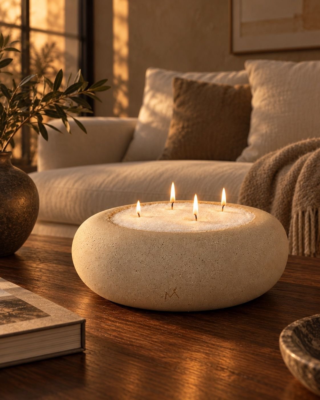 A low ivory ceramic vessel holding lit candles on a wooden table in a living room