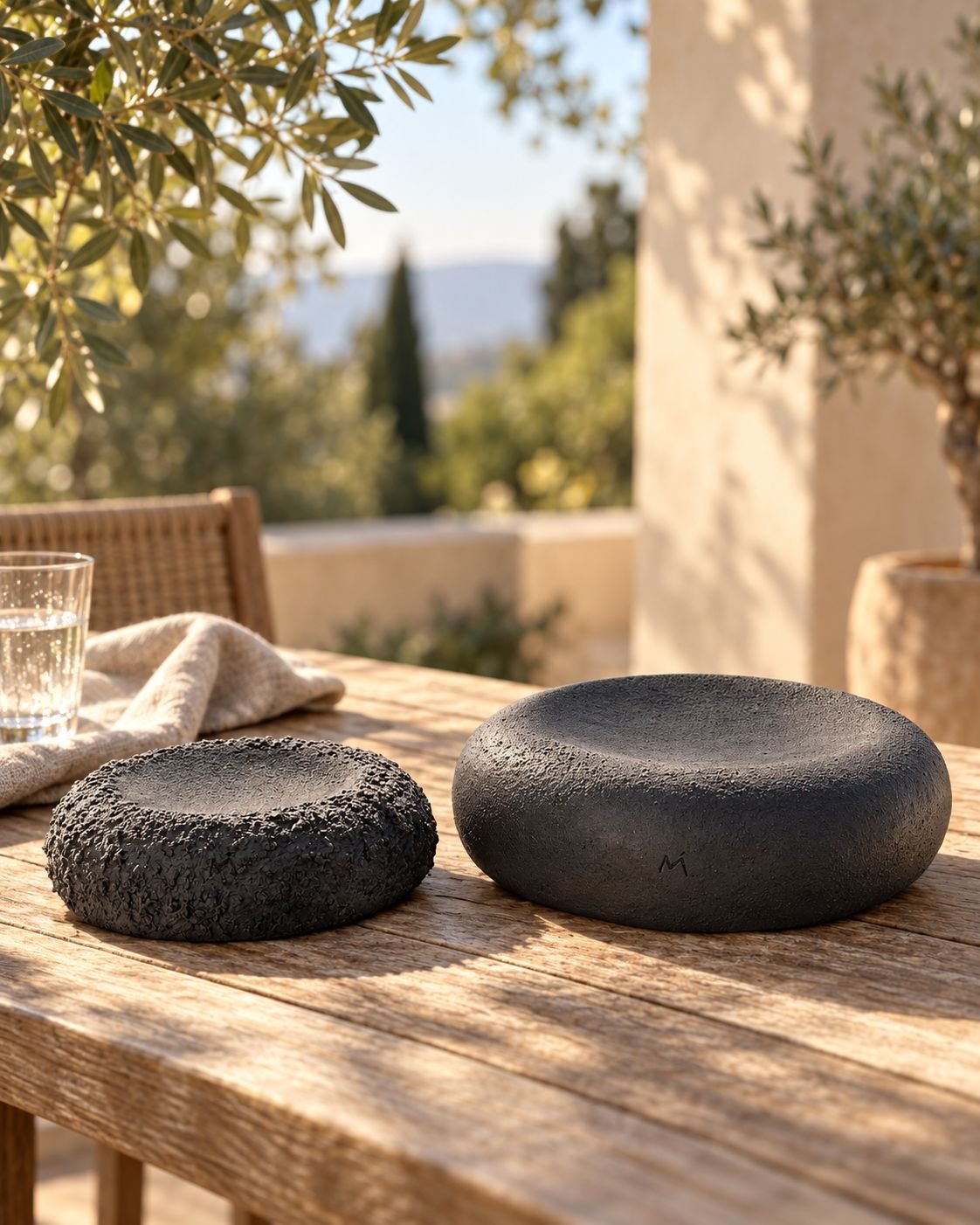 Two round charcoal ceramic forms with textured surfaces on an outdoor wooden table