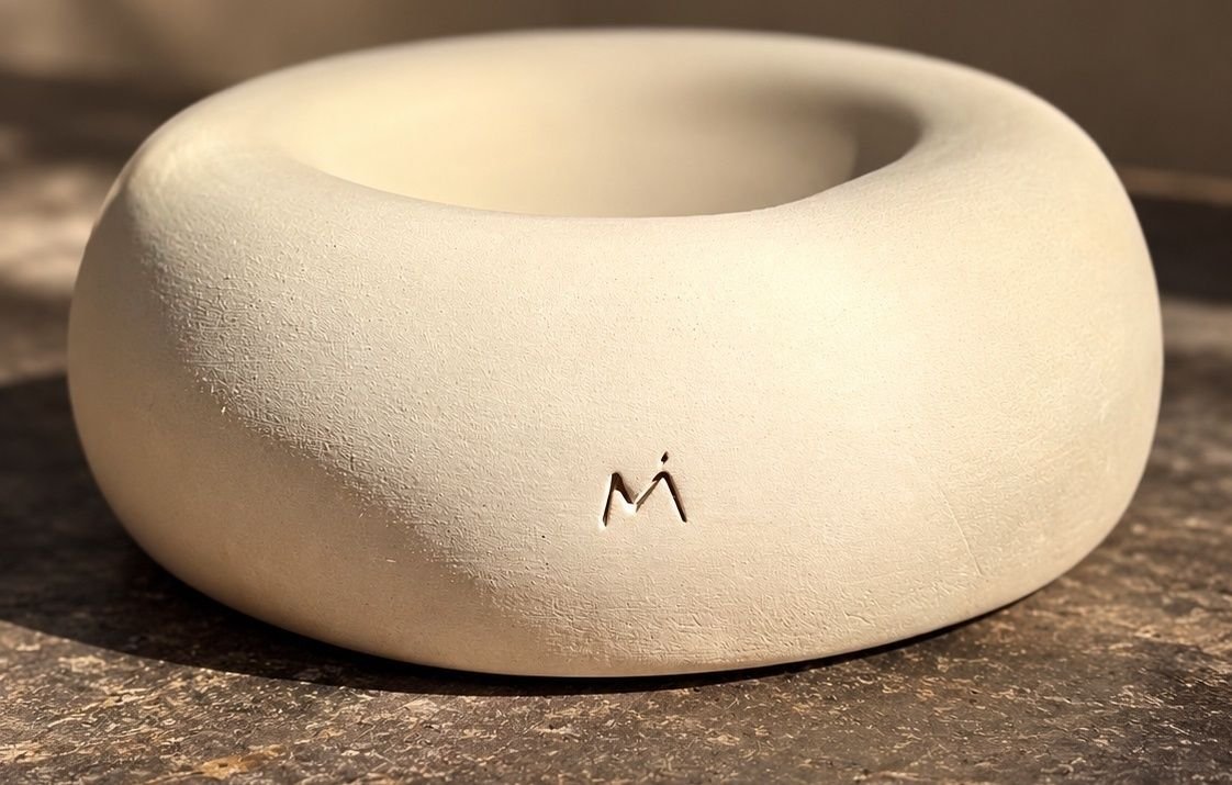 Close-up of a rounded ivory ceramic vessel with a textured surface and the MARÍA MARÍA mark