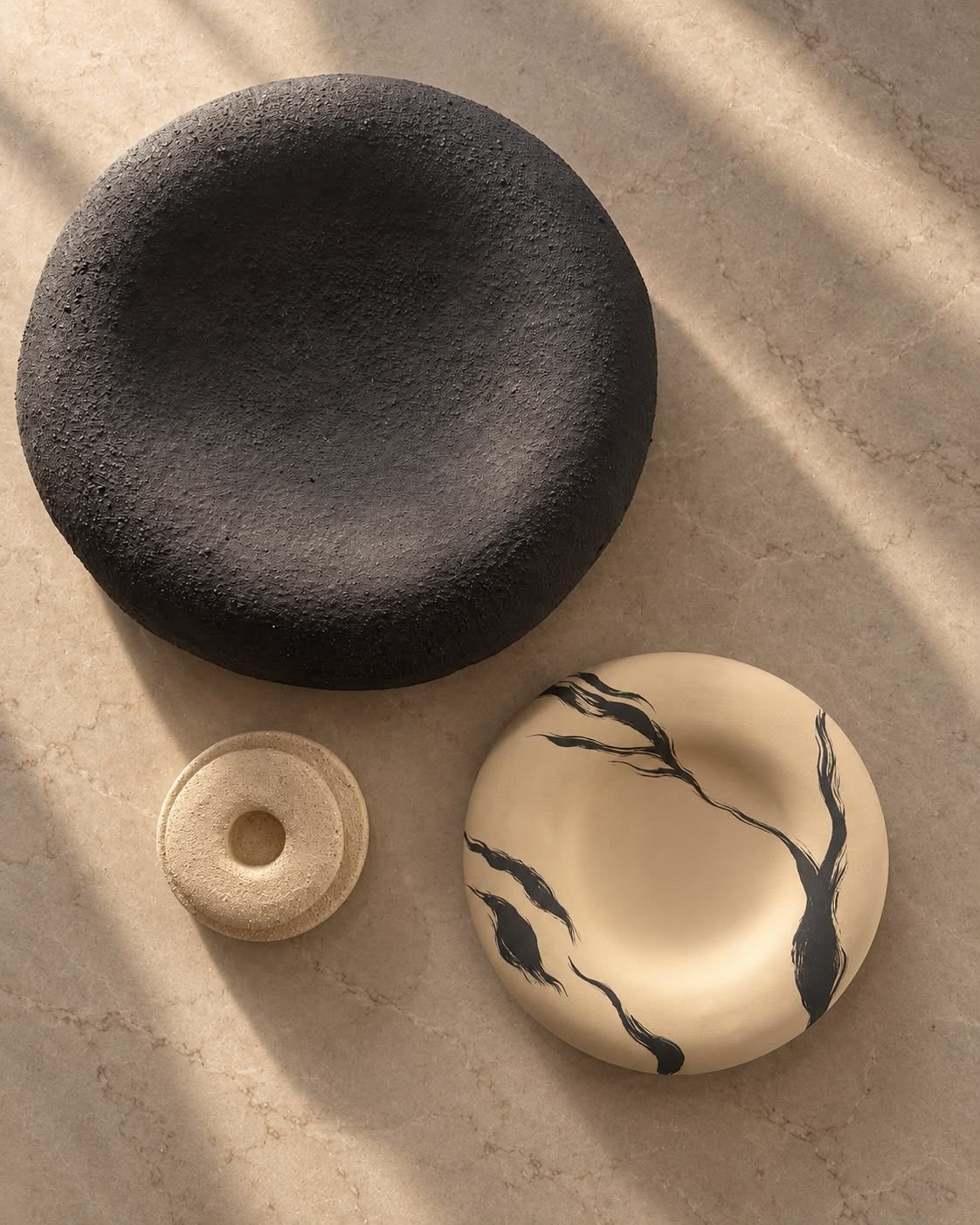 Overhead view of a black textured disc, a small ring and an ivory plate with black veining