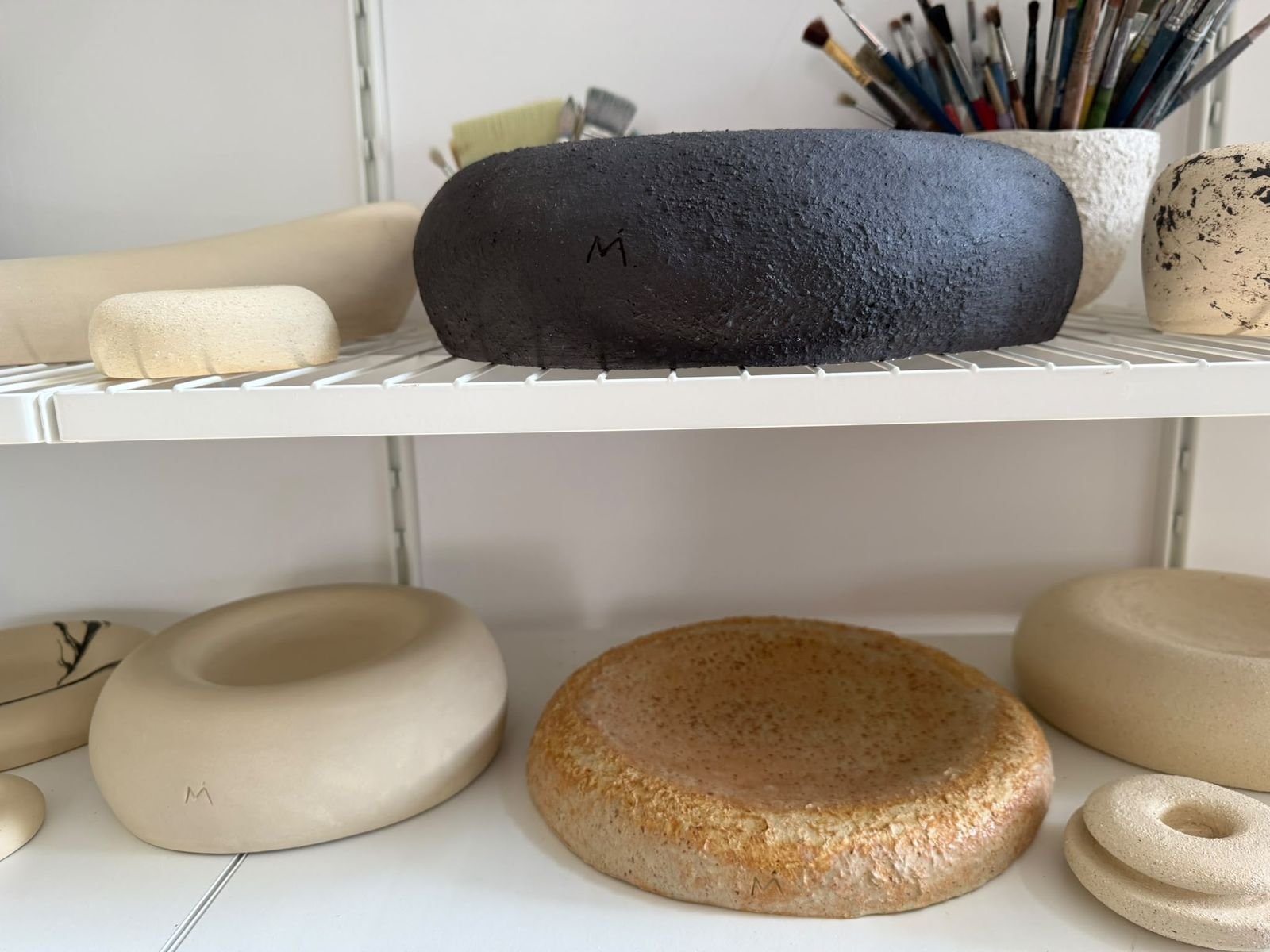 Studio shelves filled with ivory, black and marbled ceramic pieces